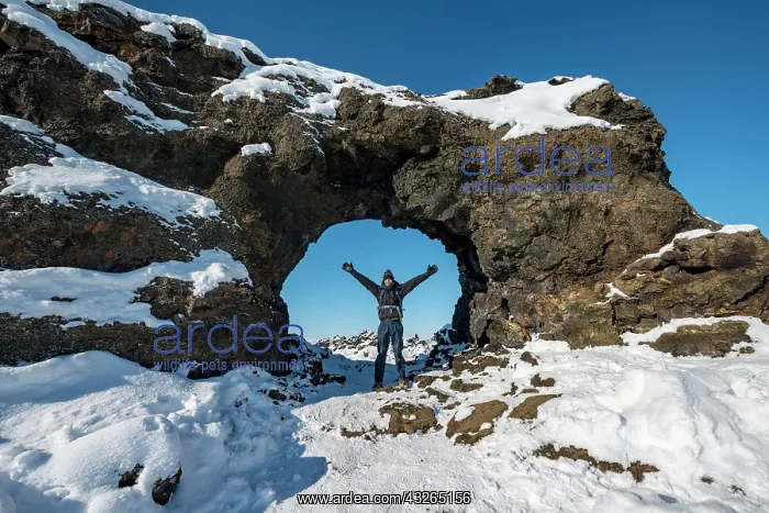 : Man standing in front of a rocky arch, lava field : Man standing in front of a rocky arch, lava field