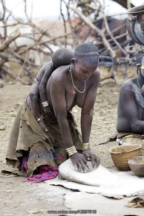 : Mursi people - woman preparing food with baby sleeping : Mursi people - woman preparing food with baby sleeping