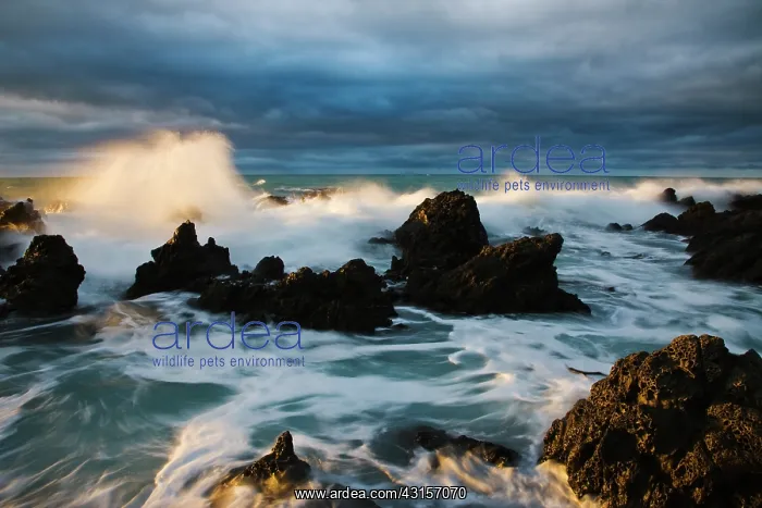 : Waves crash under dramatic sky over rocky coastline at sunri : Waves crash under dramatic sky over rocky coastline at sunri