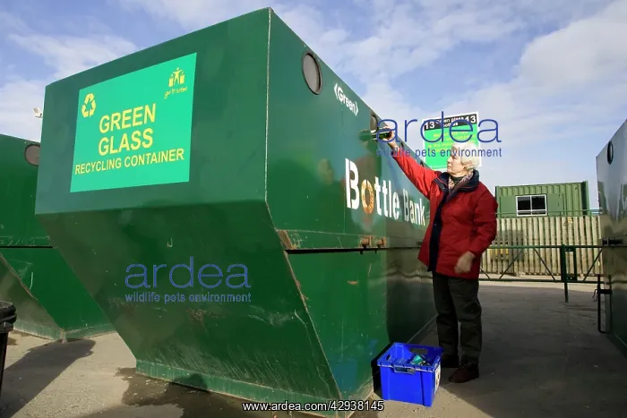  : Woman recycling glass bottle into large green skip