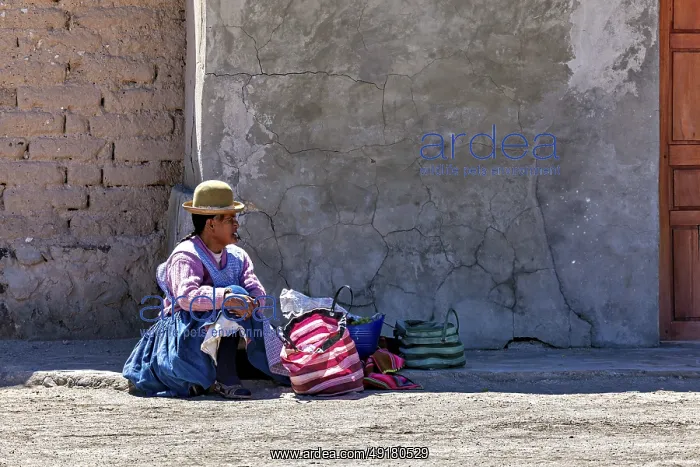 : Woman in traditional dress sitting on the floor next to colourful bags in front of a wall : Woman in traditional dress sitting on the floor next to colourful bags in front of a wall