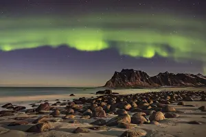 Norwegian: Aurora borealis in green colors over mountain range and coastline at night