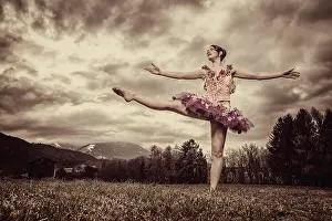 Raising: Ballerina wearing a tutu dances in front of a cloudy, g