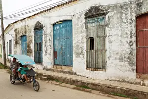 Driving: Bicycle taxi driving past decayed facades of crumbling