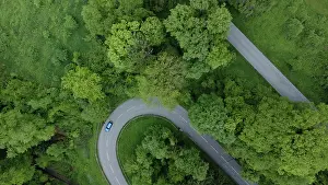 Driving: Blue car driving on serpentine road through green