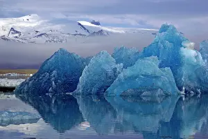 Silence: Blue iceberg reflected in calm water, mountains