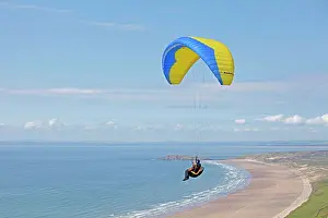 Hobbies: Blue & yellow paraglider - gliding over beach