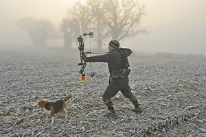 Bows: Bow hunter and his dog in a field covered with ice