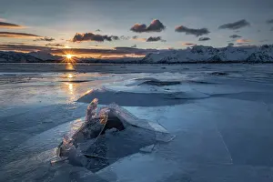 Broken: Broken ice, frozen fjord with mountains at sunset