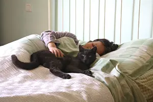 Blacks: Cat lying on a bed with a girl asleep