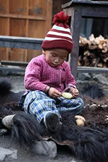 Headdress: Child peeling a potato on the skin of Yack Chame Nepal