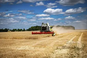 Vehicles: Combine harvester operating in a wheat field during harvest season on a sunny day with scattered clouds