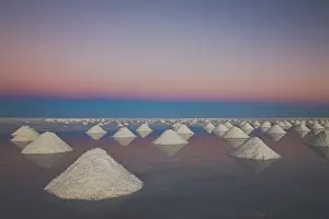 Triangle: Conical mounds of salt reflected in shallow water at sunset