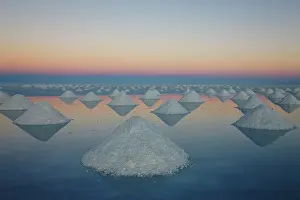 Triangle: Conical mounds of salt reflected in shallow water at sunset