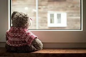 Loneliness: Cute teddy bear is sitting on the windowsill, lo