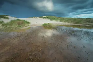 Duinen: Dark clouds above the dune valley with reflection in the wat