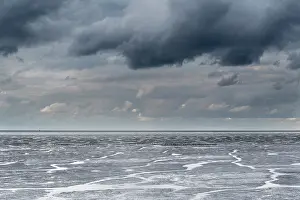 Oever: Dark clouds above the waddensea at low tide with a group of