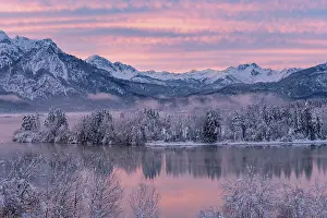Alpine Upland: Dawn and sunrise at the wintry Forggensee in a snow-covered winter landscape in the foothills of the Alps