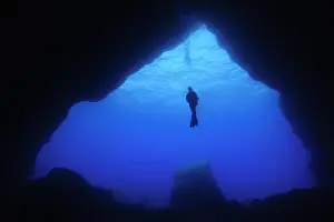 Caucasian: Diver floating in open water in front of large cave