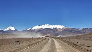 Roads: A dusty road leads through a barren landscape with snow-capped mountains in the background