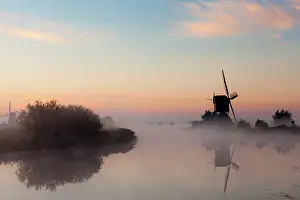 Windmill: Dutch windmill in beautiful morning light and fog with reflection in the water in Kinderdijk