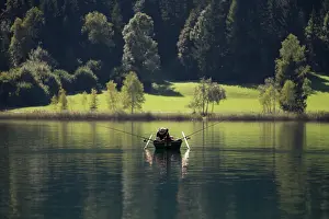 Rowing: Fisherman in a rowing boat in the morning on Weissensee