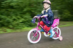 Cycling: Girl aged four wearing cycle helmet riding brightly