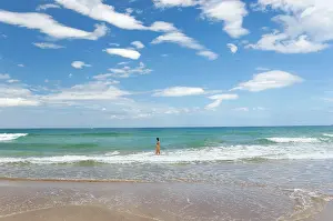 Baths: A girl baths and watches a passing boat on a beach