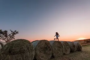 Rolls: Girl jumping on rolls of straw at sunset