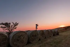 Rolls: Girl jumping on rolls of straw at sunset