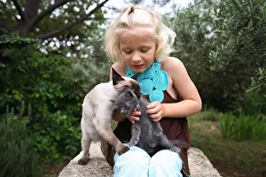 Wheedling: Girl sitting on a stone fondling two Cats
