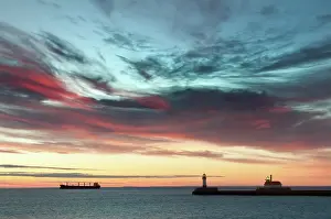 Seaport: Harbour pier with lighthouse at sunrise with a ship at the h