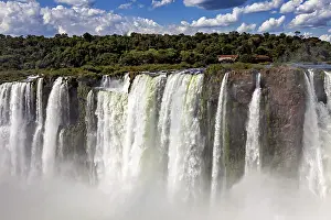 Tall: High waterfalls with rocks, spray and forested background under changing skies