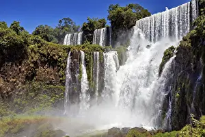 Tall: High waterfalls surrounded by lush vegetation under a bright blue sky