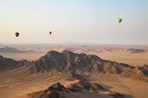 Remote: Three hot-air balloons above an arid plain and isolated mountain ridges at the edge of the Namib Desert