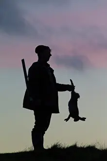 Agai: Hunter hare Hunter with dead brown Hare silhouetted agai