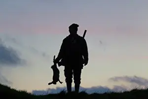 Agai: Hunter hare Hunter with dead brown Hare silhouetted agai