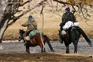 Vale: Hunters on horseback crossing a river Kyrgyzstan