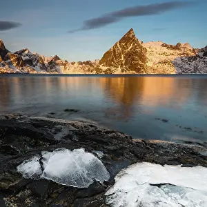 Lofoten: Ice sheets on dark rock with lake and snow-clad s