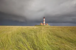 Tower: Illuminated Westerheversand lighthouse on the North Sea under dark storm clouds