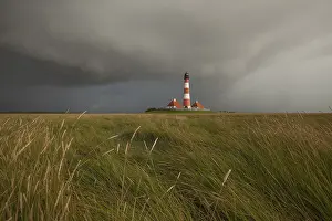 Tower: Illuminated Westerheversand lighthouse on the North Sea under dark storm clouds