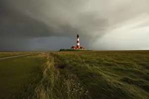 Tower: Illuminated Westerheversand lighthouse on the North Sea under dark storm clouds