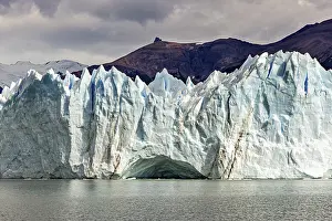 Glaciers: Impressive ice wall of a glacier under a cloudy sky near a mountain