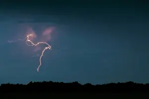 Electrical: Lightning bolt over a forest skyline by night