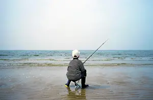 Bodies: Little boy sitting on a stool fishing, empty beach