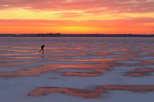 Peat: Lone skater skates on a frozen lake at sunset