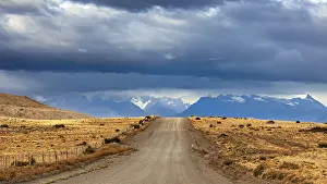 Roads: A long gravel road leads to a distant mountain range under a cloudy sky