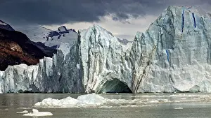 Glaciers: Majestic glacier in the water with dramatic clouds and mountains in the background