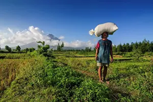 Luzon: Man with bag of rice on his head before volcano