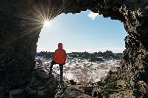 Igneous: Man in a rock arch with sunbeams, volcanic landscape